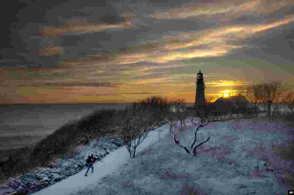 A tripod-toting photographer looks for a spot to capture the early-morning light at Portland Head Light, in Cape Elizabeth, Maine, USA. 