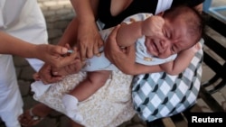 A mother holds her baby as he receives a pneumococcal vaccination during a national vaccination campaign in Managua, April 15, 2013.
