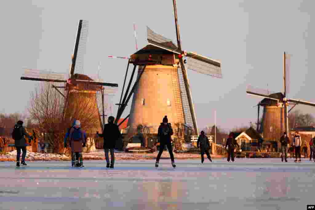 Skaters glide on the ice near windmills in the village of Kinderdijk, Netherlands.