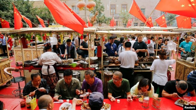 人们在新疆喀什老城区飘扬的中国国旗下吃饭 （2018年9月6日）