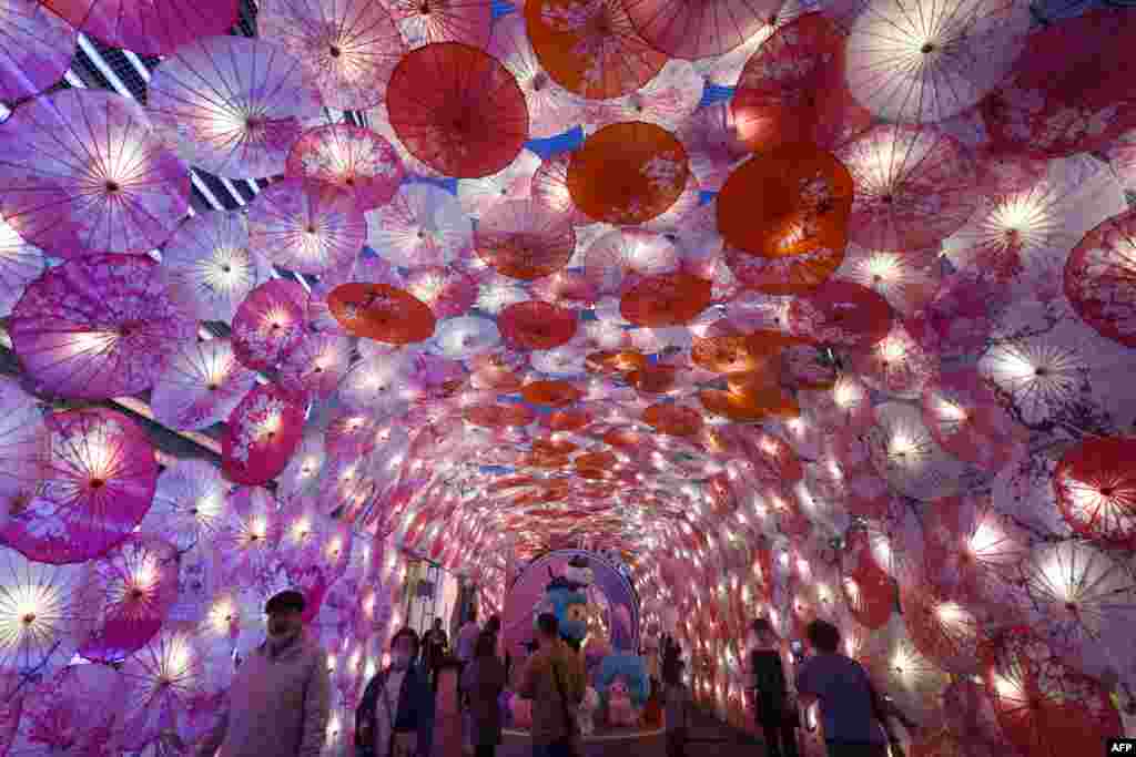 People walk past a display of umbrellas decorated with lights for the upcoming Lantern Festival on a commercial street in Hangzhou, in eastern China&#39;s Zhejiang province, Feb. 22, 2021.