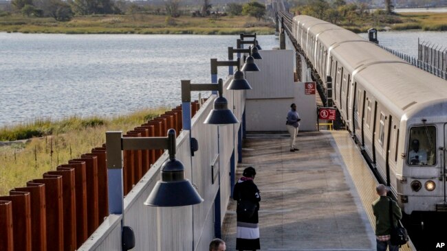 FILE - A subway train slows as it makes its way into the Broad Channel station next to a seawall installed after Superstorm Sandy washed out sections of the tracks in October 2012, in the Rockaways section of Queens, New York, on Oct. 21, 2014.