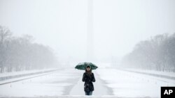 The Washington Monument and the Reflecting Pool are visible behind Claudia Marusanici as she makes her way towards the Lincoln Memorial on the National Mall, March 5, 2015, in the falling snow.