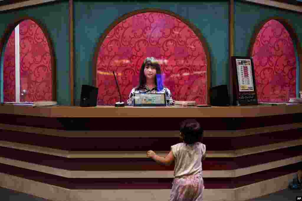 A baby girl looks at a humanoid robot sitting in a box office in Tokyo.