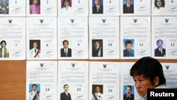 An official sits in front of a board with lists of candidate as she waits for voters at a polling station in Bangkok during a vote to elect a new Senate March 30, 2014.