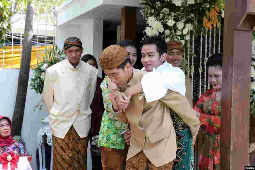 Presiden Indonesia Joko Widodo (tengah) menggendong anaknya Gibran Rakabumi sementara ibu negara Iriana Joko Widodo (kanan) tersenyum saat pesta pernikahan Rakabumi di Solo, Indonesia, Jawa Tengah. (Foto: Antara)