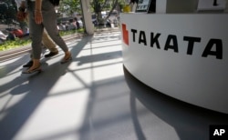 FILE - Visitors walk by a Takata Corp. desk at an automaker's showroom in Tokyo.