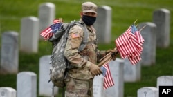 Wearing a face mask, a member of the 3rd U.S. Infantry Regiment also known as The Old Guard, places flags in front of each headstone for "Flags-In" at Arlington National Cemetery in Arlington, Va., Thursday, May 21, 2020. (AP Photo/Carolyn Kaster)