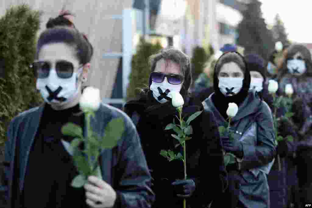 Women in black clothing with their mouths sealed with a tape walk down the street with white roses in Minsk as they protest against the verdict against the Belarusian journalist and doctor who were sentenced to jail for disclosing the medical records of a protester who died after being detained.&nbsp;