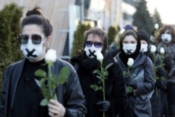 FILE - Women in black clothing with their mouths sealed with a tape walk down the street with white roses in Minsk, March 2, 2021, as they protest the verdict against a Belarusian journalist and doctor who were sentenced to jail.