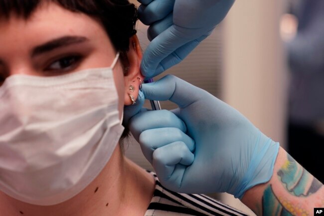 Maddie McFarland receives an ear piercing in Ann Arbor Michigan. (AP Photo/Carlos Osorio)