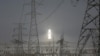 FILE - A molten salt solar tower stands behind electricity pylons at a power station near Dunhuang, Gansu province, China, April 13, 2021.