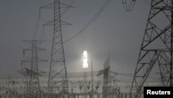 FILE - A molten salt solar tower stands behind electricity pylons at a power station near Dunhuang, Gansu province, China, April 13, 2021.