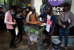 A woman wearing a face mask to curb the spread of coronavirus buys chicken on a crowded sidewalk in Pretoria, South Africa, Nov. 27, 2021.