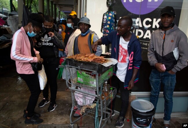 A woman wearing a face mask to curb the spread of coronavirus buys chicken on a crowded sidewalk in Pretoria, South Africa, Nov. 27, 2021.