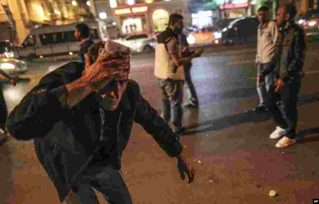 An injured man covers his forehead while Turkish riot police clash with protesters in Istanbul, Turkey, Oct. 7, 2014.