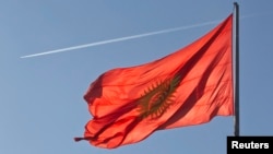 An airplane trace is seen behind a Kyrgyzstan national flag fluttering in a central square in the country's capital Bishkek.