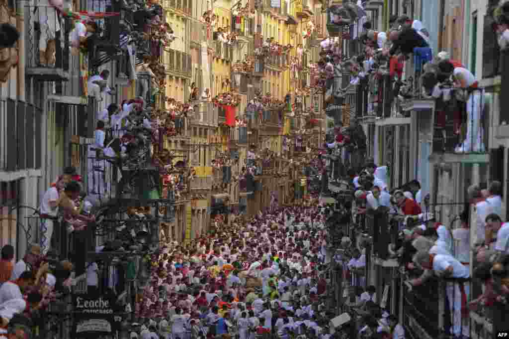 People standing on balconies look at participants as they run in front of Alcurrucen's bulls during the first bull run of the San Fermin Festival, on July 7, 2013, in Pamplona, northern Spain. The festival is a symbol of Spanish culture that attracts thou