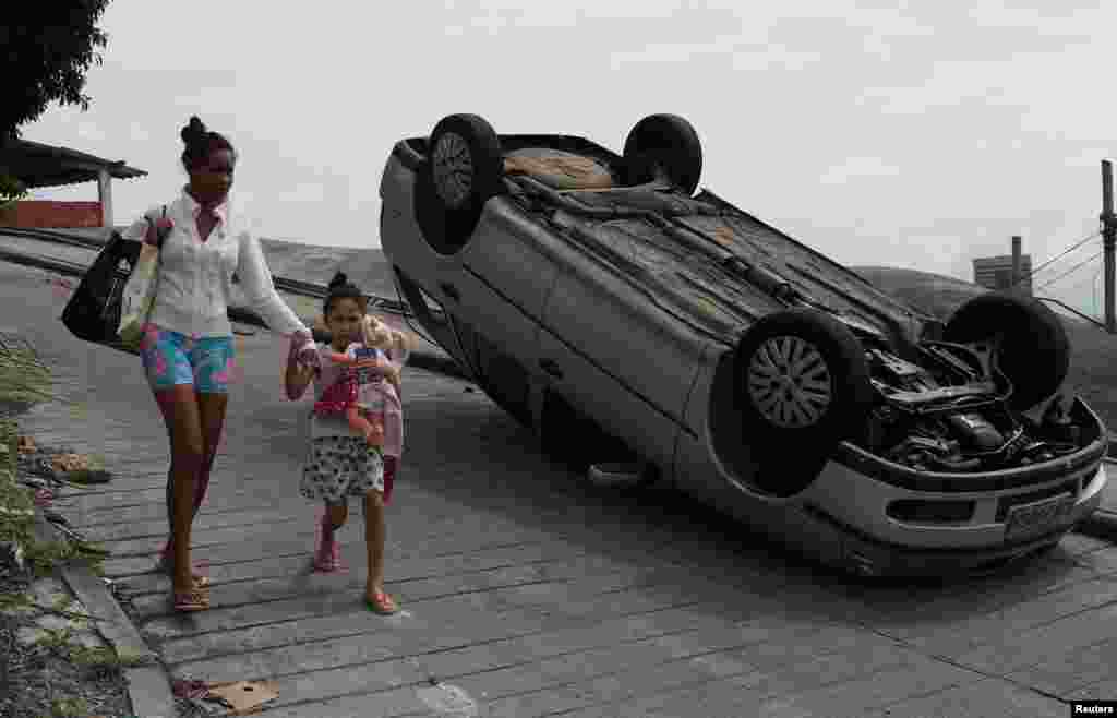 Residents walk past a car, which according to its owner was damaged during violent clashes between police and drug gangs during an operation in the Sao Carlos housing complex in Rio de Janeiro, Brazil, Aug. 28, 2018.