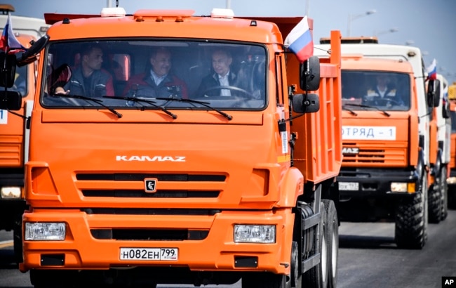 Russian President Vladimir Putin (C-R) drives a truck to officially open the much-anticipated bridge linking Russia and the Crimean peninsula, during the opening ceremony near in Kerch, Crimea, May 15, 2018.