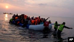 Volunteers help migrants and refugees on a dingy as they arrive at the shore of the northeastern Greek island of Lesbos, after crossing the Aegean sea from Turkey, March 20, 2016. (AP Photo/Petros Giannakouris)