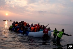 FILE - Volunteers help migrants and refugees on a dingy as they arrive at the shore of the northeastern Greek island of Lesbos, after crossing the Aegean sea from Turkey, March 20, 2016.
