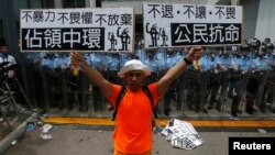 Một người biểu tình cầm áp phích 'Chiếm lĩnh Trung tâm' (trái) và 'Bất tuân Dân sự' đứng trước lực lượng cảnh sát chống bạo động bên ngoài trụ sở chính phủ ở Hồng Kông, 27/9/2014.