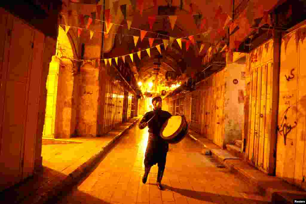 A Palestinian Musharati wearing a mask beats a drum to wake Muslims up to have the predawn meal before they start their long-day fast during the holy month of Ramadan in Nablus, in West Bank.