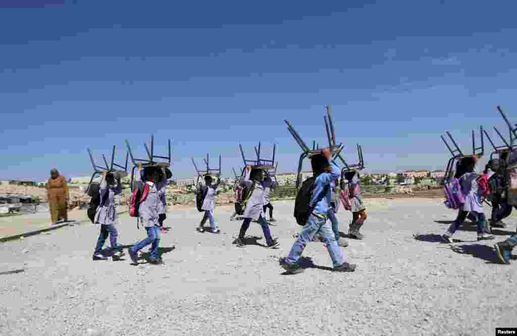 Palestinian Bedouin students carry their chairs to a tent after attending a class outdoors near the Jewish settlement of Maale Adumim, in the West Bank village of Al-Eizariya, east of Jerusalem.