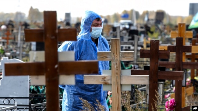 A grave digger wearing a protective suit stands during a a COVID-19 victim burial at a cemetery outside in Omsk, Russia, Oct. 7, 2021.