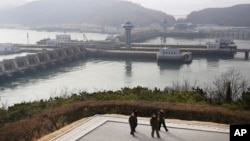 North Korean men walk with the West Sea Barrage in the background in Nampo, North Korea, Feb. 2, 2019.