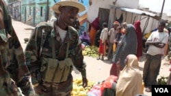 Women sell fruit at a market in Bala'ad, Somalia on July 3, 2012, as soldiers stand guard. (VOA/M. Yusuf)