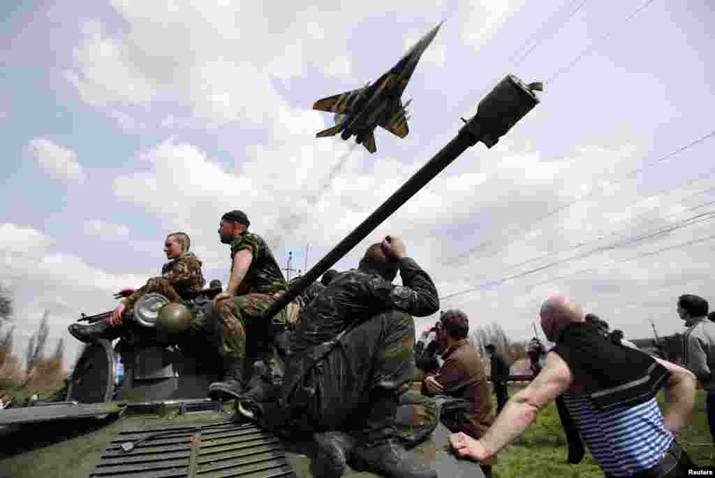 Um avião de guerra passa por cima de soldados ucranianos sentados em cima de um carro blindado em Kramatorsk, Ucrânia.