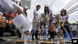 A Thai volunteer, left, pours detergent as others sweep a road during a cleaning drive after flood waters receded in Bangkok, Thailand, November 20, 2011.