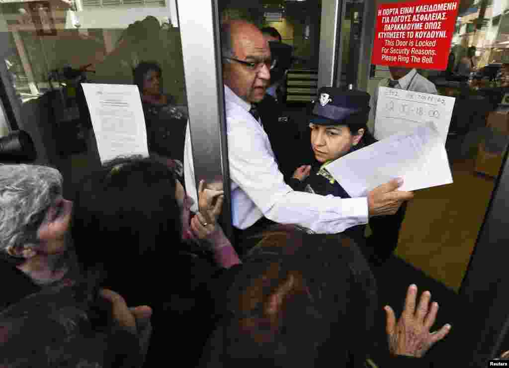 2013年3月28日，一名莱基银行的管理人员帮助一名警察从人群中挤过进入银行。大批储户在莱基银行在塞浦路斯尼科西亚的这家支行外排队等候。
