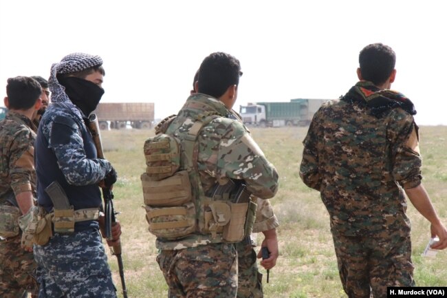 Internationally-backed Syrian Democratic Forces watch as trucks filled with people evacuate Baghuz, IS's last stronghold in Syria on Feb. 26, 2019, near Baghuz.