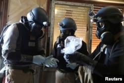 A U.N. chemical weapons expert, wearing a gas mask, holds a plastic bag containing samples from one of the sites of an alleged chemical weapons attack in the Ain Tarma neighborhood of Damascus, Syria, Aug. 29, 2013.