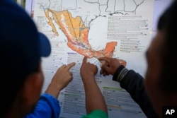 Migrants discuss their journey using a map posted inside the sports complex where thousands of migrants have been camped out for several days in Mexico City, Nov. 9, 2018.