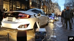 People look at Honda's new fuel cell vehicle "Clarity" that is distributing its hydrogen fuel cell power to illuminate six trees along the street in Tokyo's Marunouchi office and shopping district in Tokyo Friday, Dec. 25, 2015. (AP Photo/Koji Sasahara)