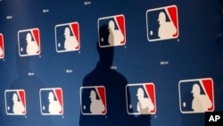 FILE - The shadow of MLB Commissioner Rob Manfred is projected on an MLB logo backdrop in Phoenix, Arizona, Feb. 23, 2015.