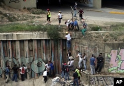 Demonstrators climb a wall to avoid Bolivarian National Guard officers who fired tear gas during a protest in Caracas, Venezuela, April 8, 2017. Opponents of President Nicolas Maduro protested on the streets of the capital as part of a movement that shows no sign of losing steam.