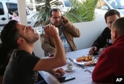 In this March 18, 2017, photo, Syrian Lt. Col. Ahmed al-Saoud, center, commander of the U.S.-backed Division 13 uses his mobile phone in a Syrian restaurant surrounded by aides and bodyguards, in Iskenderun, southern Turkey.