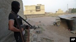 FILE - A masked anti-government gunman holds his weapon as he stands guard in Fallujah, Iraq.