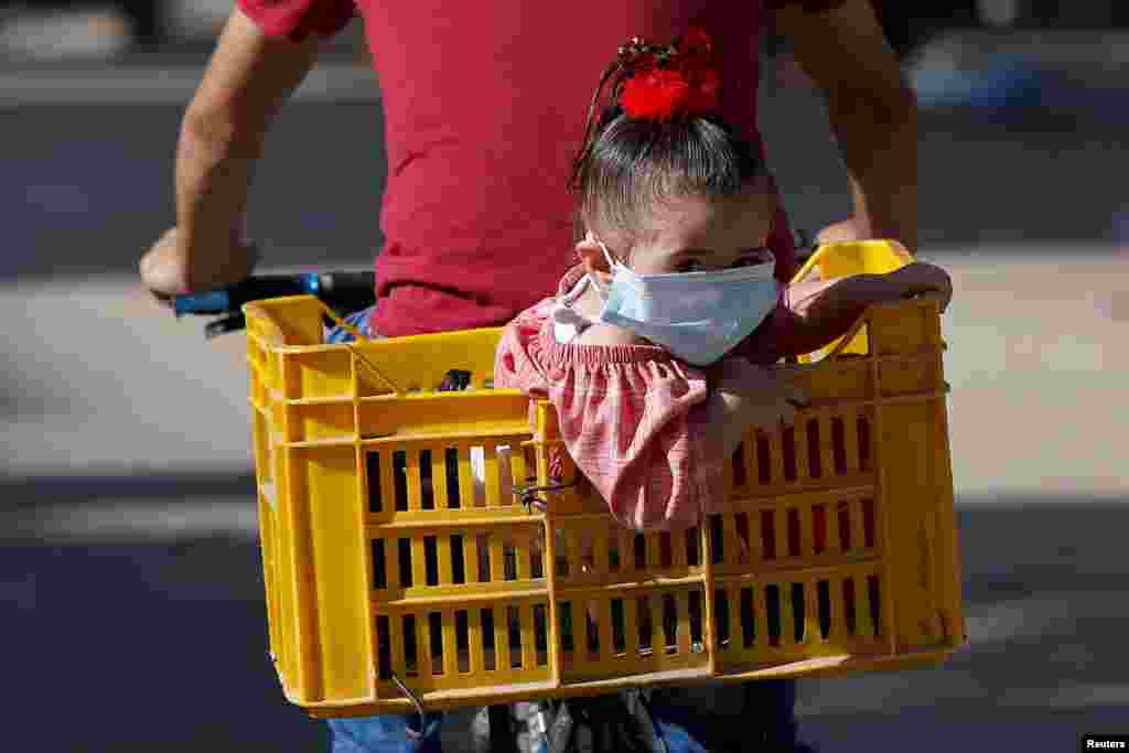 A Palestinian girl wearing a protective face mask sits in a box on the back of a bicycle amid the coronavirus disease (COVID-19) crisis, in Gaza City.