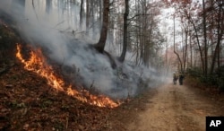 Firefighters walk down a dirt road a wildfire burns a hillside, Nov. 15, 2016, in Clayton, Georgia. The U.S. Forest Service is tracking wildfires that have burned 80,000 acres across the South.
