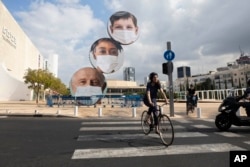 Seorang warga Israel bersepeda, melewati spanduk yang mengimbau warga untuk mengenakan masker di tengah pemberlakuan lockdown di Tel Aviv, Israel, Kamis, 24 September 2020.
