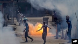 A tear gas shell fired by an Indian policeman explodes behind Kashmiri protesters during a protest in Srinagar, Indian controlled Kashmir, June 16, 2017.