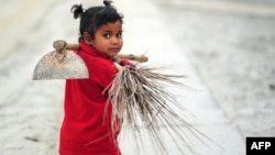FILE - Young Indian child Laxmi carries a broom and hoe as she walks with her mother after working at the site of the annual traditional fair Magh Mela at Sangam, the confluence of the rivers Ganges and Yamuna, and the mythical Saraswati in Allahabad on January 2, 2015.