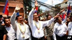 Cambodia's opposition leader Sam Rainsy, center, of the Cambodia National Rescue Party waves along with his party Vice President Kem Sokha, third from left, during a march in Phnom Penh, Cambodia, Sunday, March 30, 2014.