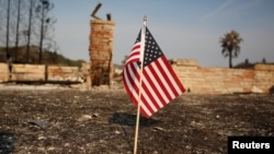 FILE - An American flag stands in front of a home destroyed after a wildfire tore through Santa Rosa, California, Oct. 15, 2017.